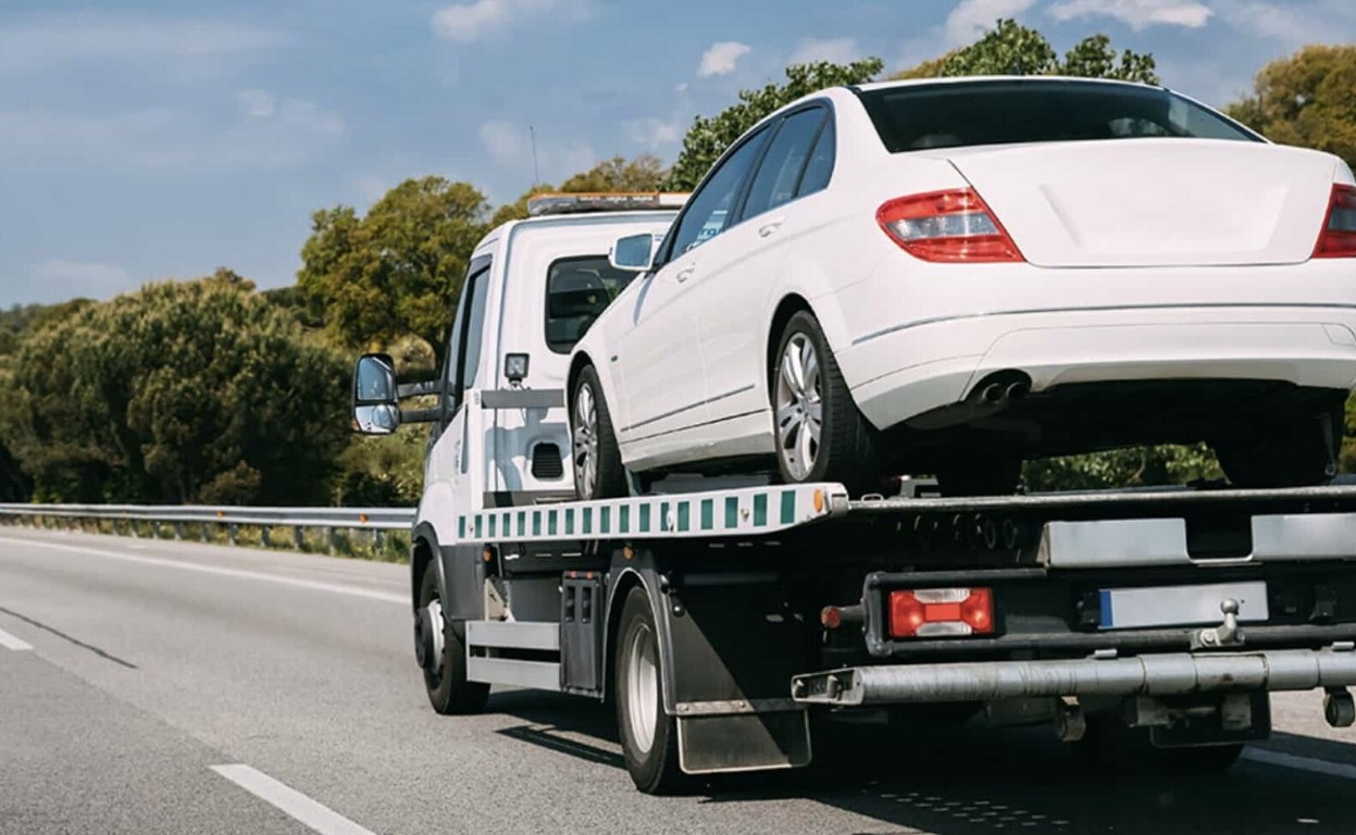 White car on a flatbed tow truck for long distance towing on a highway in West Babylon, NY