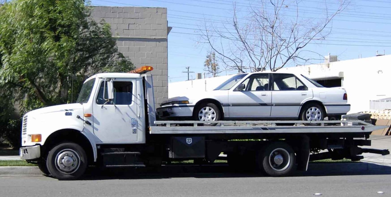 White flatbed tow truck transporting a sedan in North Babylon, NY